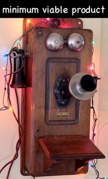 Photo of antique hand crank telephone on wall with Christmas lights around it for the holidays.
